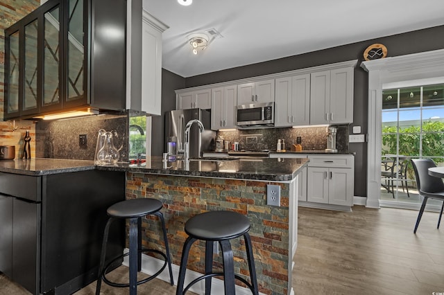 752 Hobonny Loop, Longs, SC 29568 - kitchen with stainless steel appliances, a peninsula, glass insert cabinets, a kitchen bar, and dark stone counters