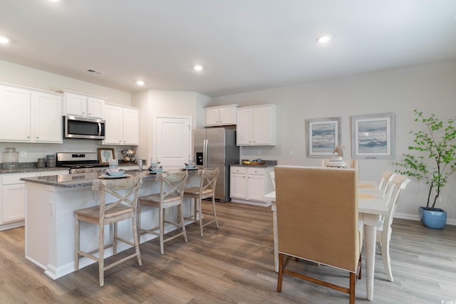 1402 Nokota Dr, Conway, SC 29526 - kitchen featuring appliances with stainless steel finishes, wood finished floors, a kitchen island with sink, white cabinetry, and a breakfast bar