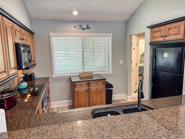145 Hartland Dr Unit 4-E, Myrtle Beach, SC 29572 - kitchen featuring black appliances, a textured ceiling, wood finished floors, brown cabinetry, and dark stone countertops
