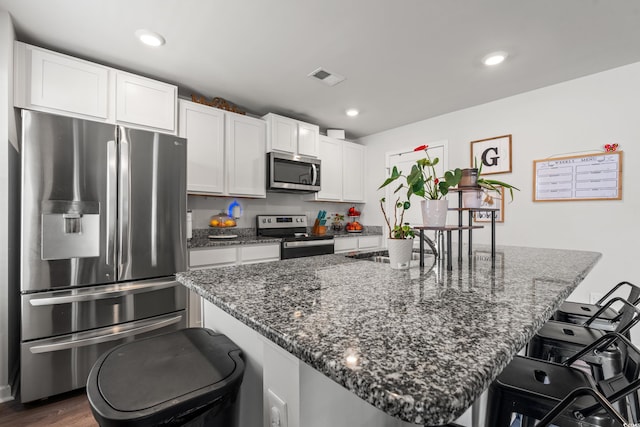 190 Belmonte Dr, Myrtle Beach, SC 29588 - kitchen with stainless steel appliances, a kitchen breakfast bar, white cabinetry, dark stone countertops, and a center island with sink