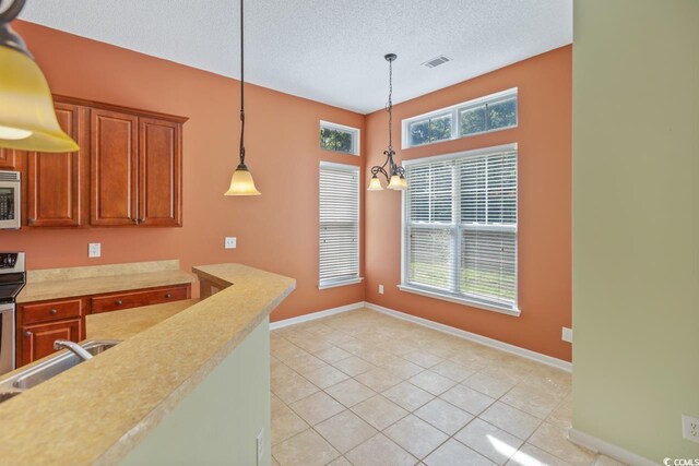 56 Willowbend Dr, Murrells Inlet, SC 29576 - kitchen with light countertops, hanging light fixtures, light tile patterned floors, brown cabinetry, and stainless steel microwave