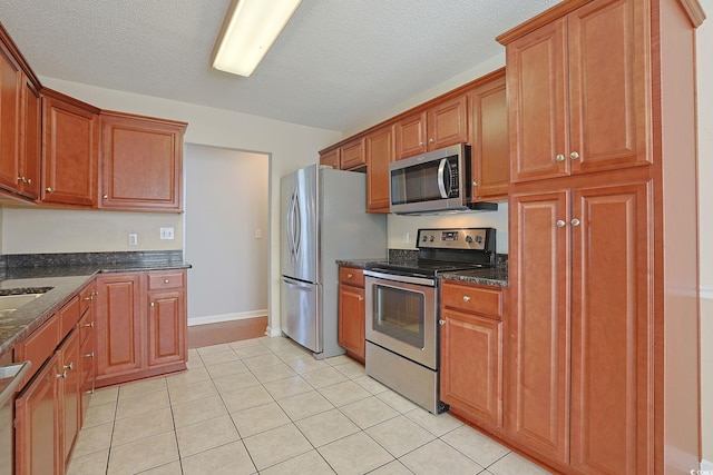 3888 Stillwood Dr, Myrtle Beach, SC 29588 - kitchen with stainless steel appliances, light tile patterned floors, dark stone countertops, brown cabinets, and a textured ceiling
