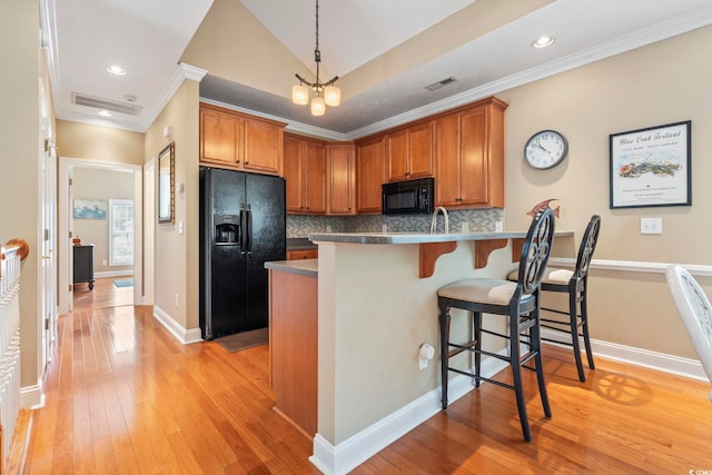 670 2nd Ave N, North Myrtle Beach, SC 29582 - kitchen featuring black appliances, light wood-style floors, a peninsula, a kitchen bar, and tasteful backsplash