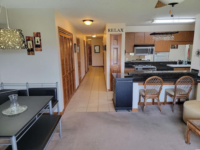 207 Double Eagle Dr Unit E-1, Surfside Beach, SC 29575 - kitchen with stainless steel microwave, brown cabinetry, light colored carpet, dark countertops, and a breakfast bar area