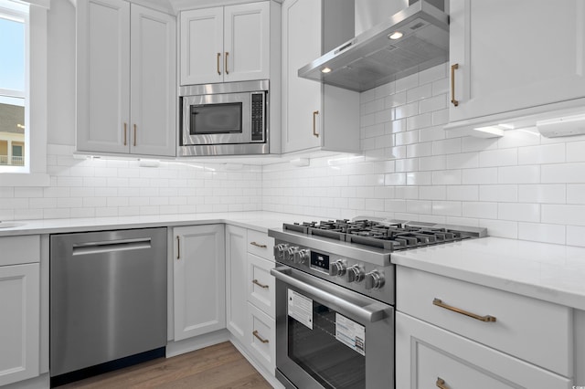 8148 Living Tide Dr, Myrtle Beach, SC 29572 - kitchen featuring appliances with stainless steel finishes, wall chimney range hood, backsplash, white cabinets, and wood finished floors