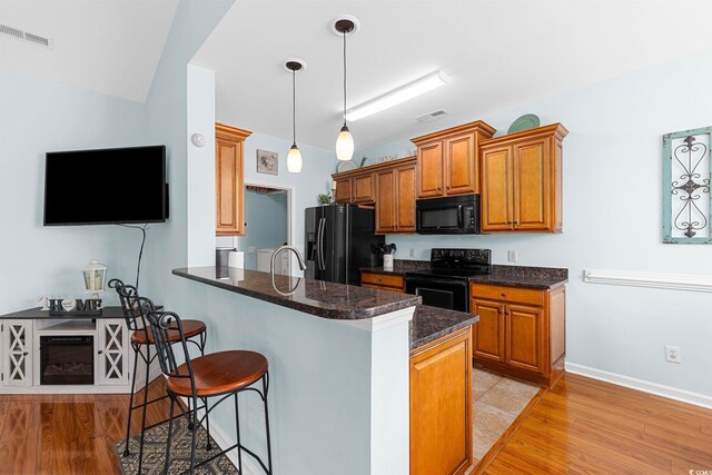 755 Wintercreeper Dr, Longs, SC 29568 - kitchen with black appliances, a breakfast bar, brown cabinets, a peninsula, and light wood-style floors