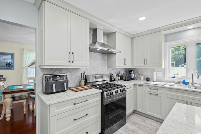 528 George Washington Trl, Georgetown, SC 29440 - kitchen featuring wall chimney exhaust hood, stainless steel gas range oven, light wood finished floors, backsplash, and white cabinetry