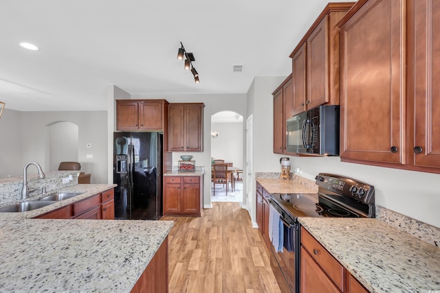 1276 Brighton Hill Ave, Myrtle Beach, SC 29588 - kitchen featuring arched walkways, black appliances, light wood-style floors, brown cabinetry, and light stone countertops