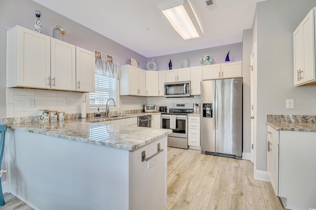6203 Catalina Dr Unit 935, North Myrtle Beach, SC 29582 - kitchen featuring appliances with stainless steel finishes, a peninsula, light stone counters, light wood finished floors, and backsplash