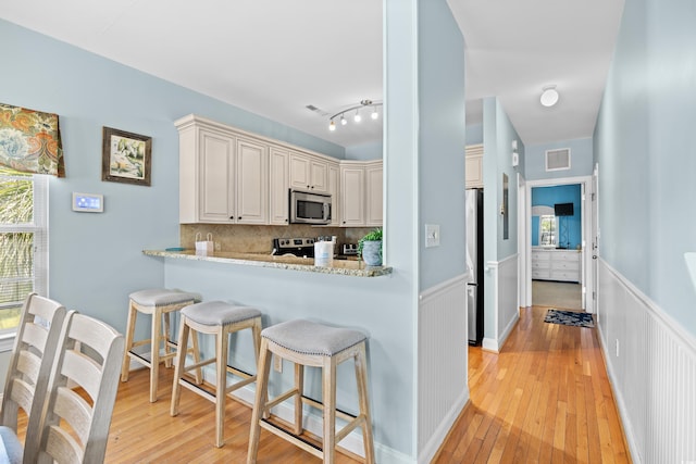 1020 Ocean Blvd S Unit A, Surfside Beach, SC 29575 - kitchen featuring stainless steel appliances, light wood-type flooring, a wainscoted wall, a breakfast bar, and decorative backsplash