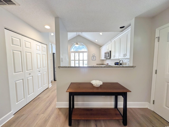 50 Pawleys Place Dr Unit 50, Pawleys Island, SC 29585 - kitchen with stainless steel microwave, light wood-style flooring, white cabinetry, vaulted ceiling, and a textured ceiling