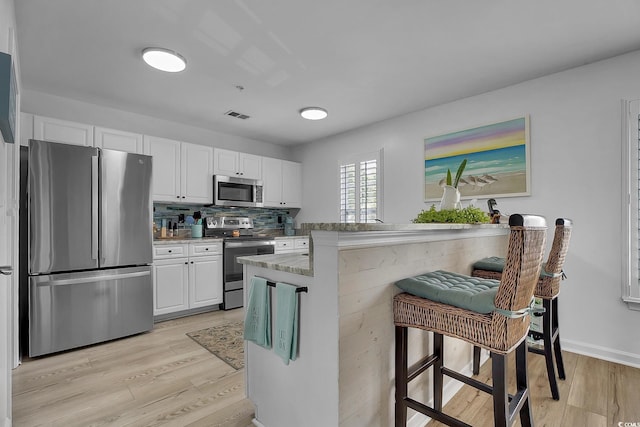 139 Butkus Dr Unit 3, Myrtle Beach, SC 29588 - kitchen featuring stainless steel appliances, light wood-style flooring, white cabinets, a kitchen bar, and decorative backsplash
