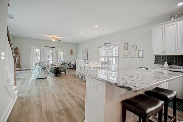 115A 8th Ave N, Surfside Beach, SC 29575 - kitchen with light wood-style flooring, a kitchen breakfast bar, white cabinetry, light stone countertops, and recessed lighting