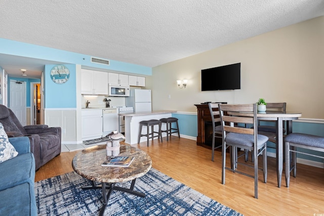 5523 N Ocean Blvd Unit 908, Myrtle Beach, SC 29577 - living room featuring light wood-type flooring, a textured ceiling, and a wainscoted wall