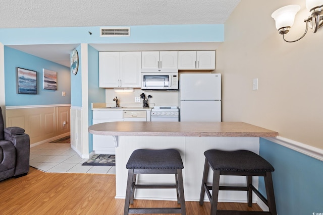 5523 N Ocean Blvd Unit 908, Myrtle Beach, SC 29577 - kitchen with white appliances, a breakfast bar, white cabinets, wainscoting, and a textured ceiling