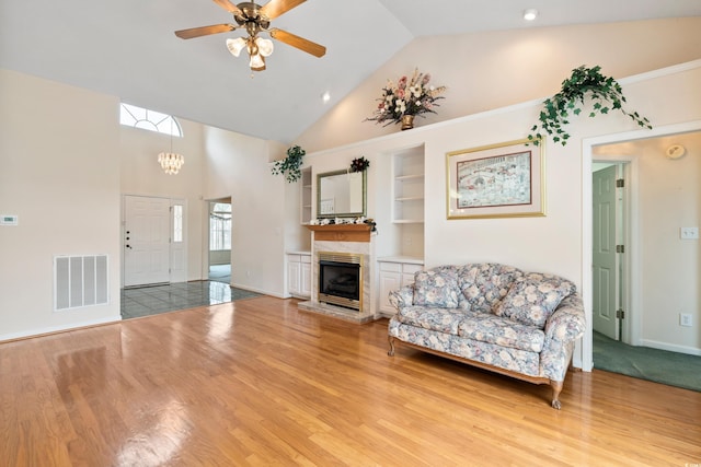 2443 Glen Dr, Little River, SC 29566 - living room featuring built in shelves, light wood-style floors, a ceiling fan, high vaulted ceiling, and a chandelier