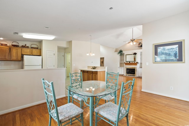 2443 Glen Dr, Little River, SC 29566 - dining area with a fireplace, light wood-style floors, ceiling fan, vaulted ceiling, and a chandelier