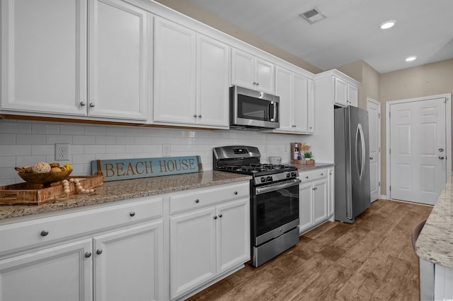 4737 Seclusion Ln, Myrtle Beach, SC 29577 - kitchen featuring appliances with stainless steel finishes, white cabinetry, wood finished floors, light stone countertops, and decorative backsplash