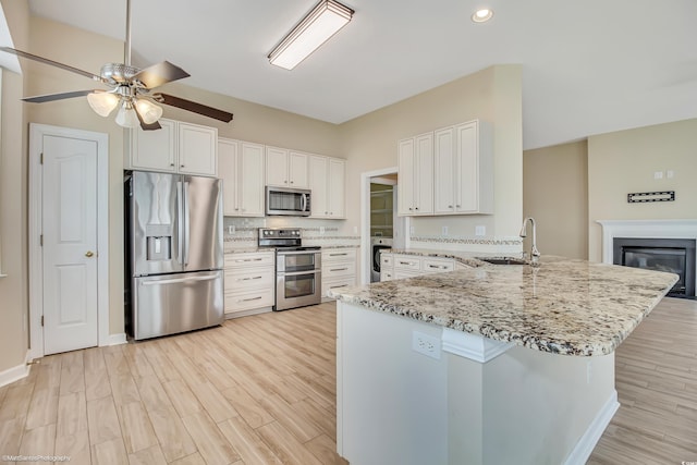2901 Whooping Crane Dr, North Myrtle Beach, SC 29582 - kitchen with stainless steel appliances, a ceiling fan, light stone countertops, light wood finished floors, and a peninsula