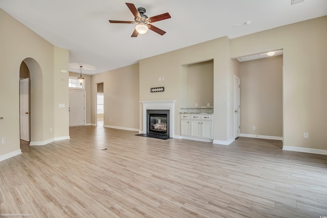 2901 Whooping Crane Dr, North Myrtle Beach, SC 29582 - unfurnished living room featuring a ceiling fan, light wood-style flooring, a fireplace with flush hearth, and arched walkways