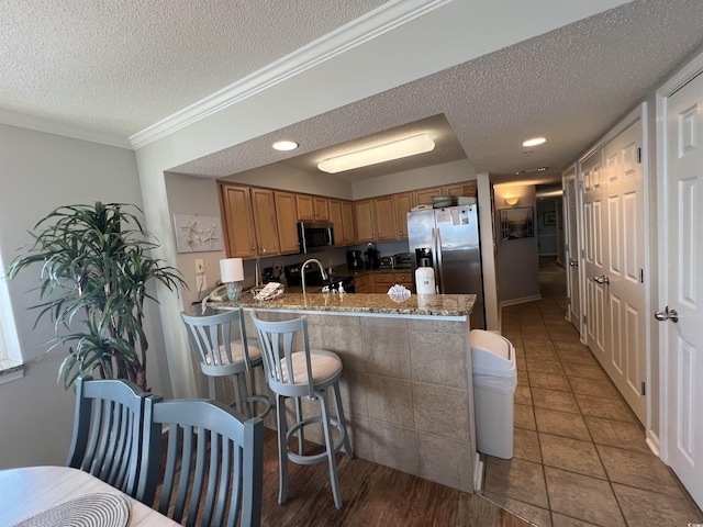 1401 S Ocean Blvd Unit 1307, North Myrtle Beach, SC 29582 - kitchen with a textured ceiling, appliances with stainless steel finishes, a peninsula, ornamental molding, and brown cabinetry
