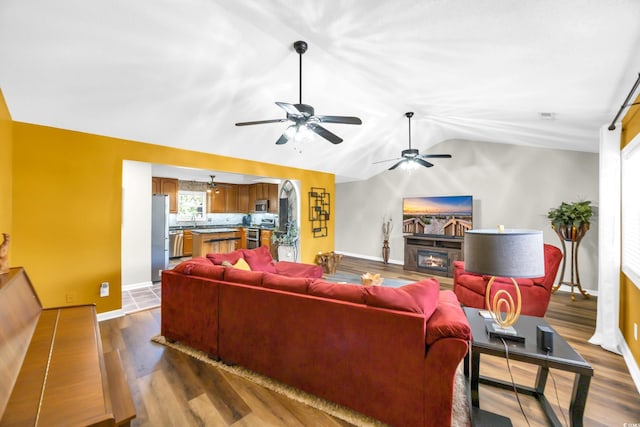 209 Chickasaw Ln, Myrtle Beach, SC 29579 - living room featuring ceiling fan, vaulted ceiling, dark wood-type flooring, a glass covered fireplace, and arched walkways