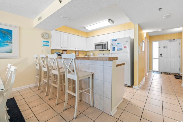5310 N Ocean Blvd Unit 7C, North Myrtle Beach, SC 29582 - kitchen with freestanding refrigerator, stainless steel microwave, light tile patterned flooring, white cabinets, and a peninsula