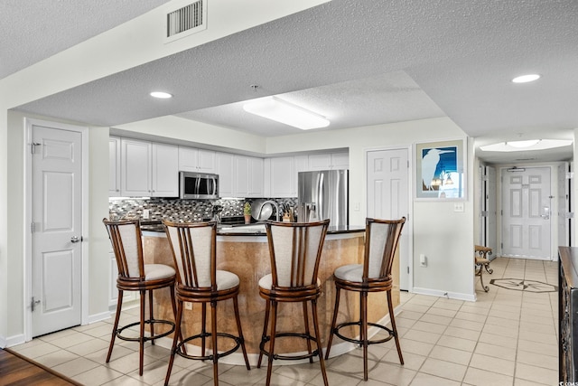 2151 Bridgeview Ct Unit 3-404, North Myrtle Beach, SC 29582 - kitchen with appliances with stainless steel finishes, a textured ceiling, white cabinets, light tile patterned floors, and a breakfast bar area
