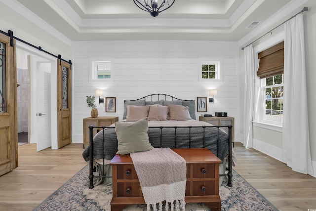 1320 James Island Ave, North Myrtle Beach, SC 29582 - bedroom featuring a barn door, a tray ceiling, light wood-style flooring, multiple windows, and crown molding