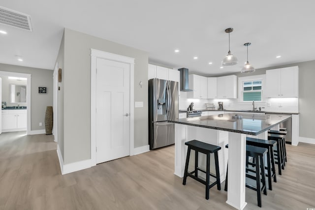 330 51st Ave N, North Myrtle Beach, SC 29582 - kitchen featuring appliances with stainless steel finishes, wall chimney exhaust hood, a kitchen breakfast bar, light wood-style flooring, and white cabinetry