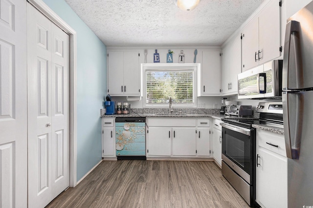 1005 28th Ave S, North Myrtle Beach, SC 29582 - kitchen featuring stainless steel appliances, wood finished floors, white cabinets, a textured ceiling, and stone countertops