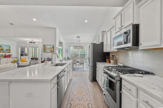 3909 On Deck Cir, Little River, SC 29566 - kitchen featuring appliances with stainless steel finishes, a center island with sink, light wood-type flooring, decorative backsplash, and white cabinetry