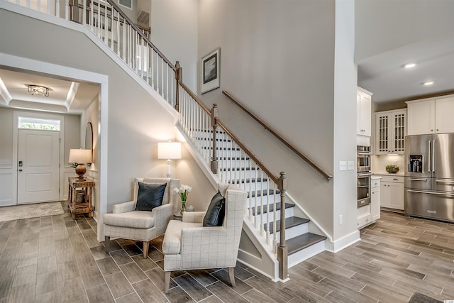 stairway featuring a high ceiling, light hardwood / wood-style floors, and a tray ceiling