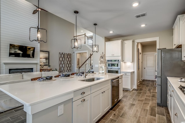 kitchen featuring white cabinets, a center island with sink, stainless steel appliances, a fireplace, and sink