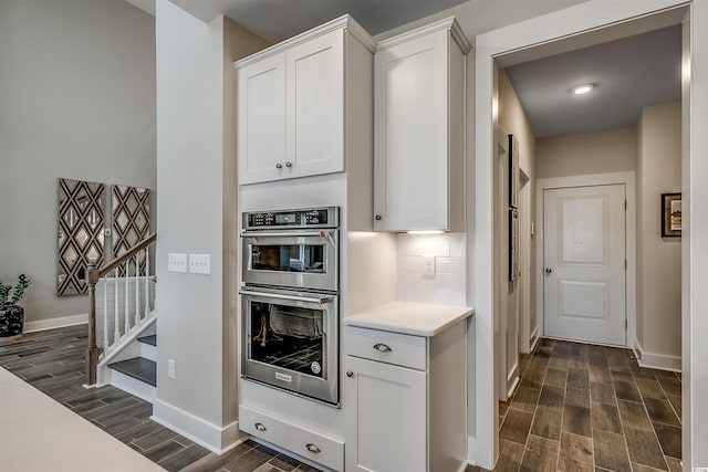 kitchen with tasteful backsplash, stainless steel double oven, dark hardwood / wood-style floors, and white cabinets