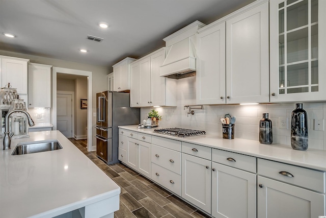 kitchen featuring custom exhaust hood, sink, stainless steel appliances, white cabinets, and tasteful backsplash