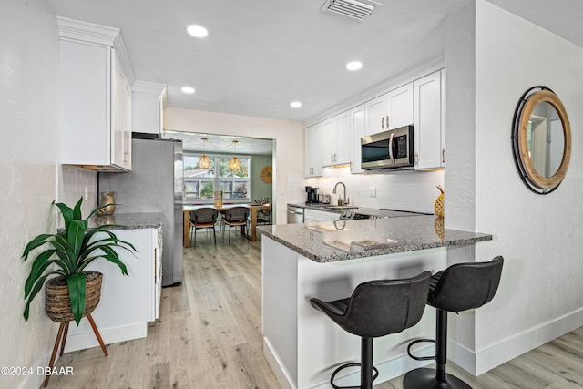 kitchen featuring white cabinets, light hardwood / wood-style floors, dark stone countertops, and appliances with stainless steel finishes