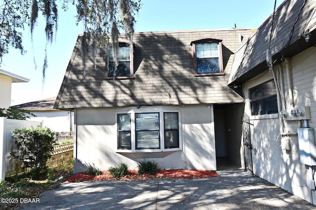 view of front of house featuring mansard roof, fence, and a shingled roof