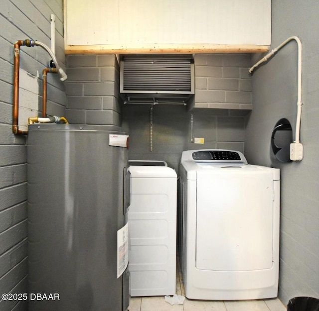 washroom with washer and dryer, water heater, light tile patterned flooring, concrete block wall, and laundry area