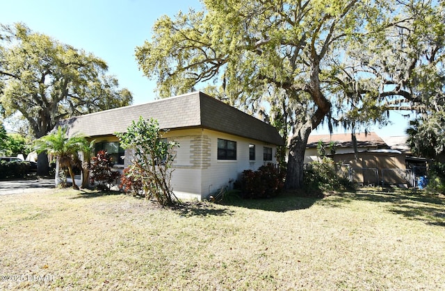 view of side of home featuring mansard roof, a yard, and roof with shingles