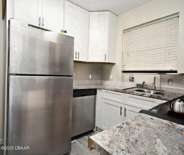 kitchen with light stone counters, appliances with stainless steel finishes, wood finished floors, white cabinetry, and a sink