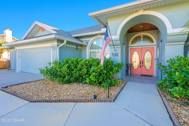 doorway to property with a garage, a shingled roof, concrete driveway, and stucco siding