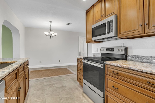 kitchen featuring visible vents, baseboards, appliances with stainless steel finishes, light stone countertops, and brown cabinetry