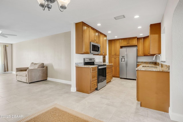 kitchen with ceiling fan, appliances with stainless steel finishes, open floor plan, light stone countertops, and a sink