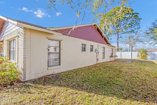 view of home's exterior with stucco siding, fence, and a lawn