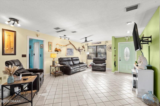 living room with light tile patterned floors, a ceiling fan, visible vents, and a textured ceiling