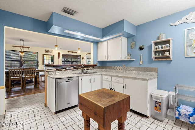 kitchen with visible vents, a peninsula, stainless steel dishwasher, white cabinets, and a sink