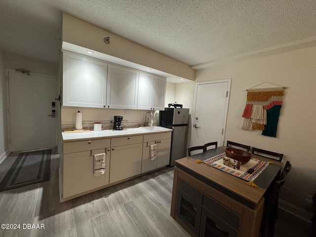 kitchen featuring light wood-type flooring, a textured ceiling, sink, white cabinetry, and stainless steel refrigerator