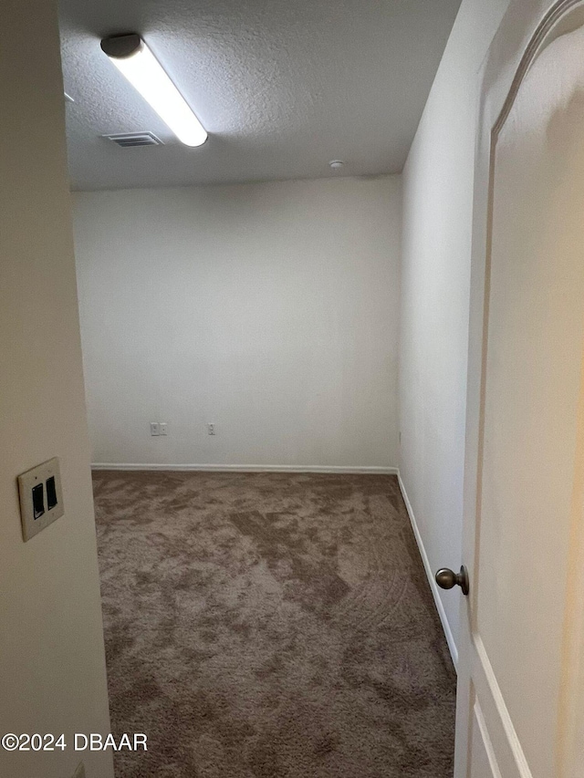 unfurnished room with dark carpet and a textured ceiling