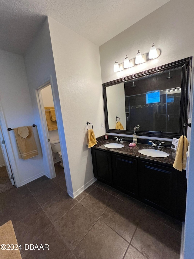 bathroom with tile patterned floors, vanity, a textured ceiling, toilet, and a shower with shower door